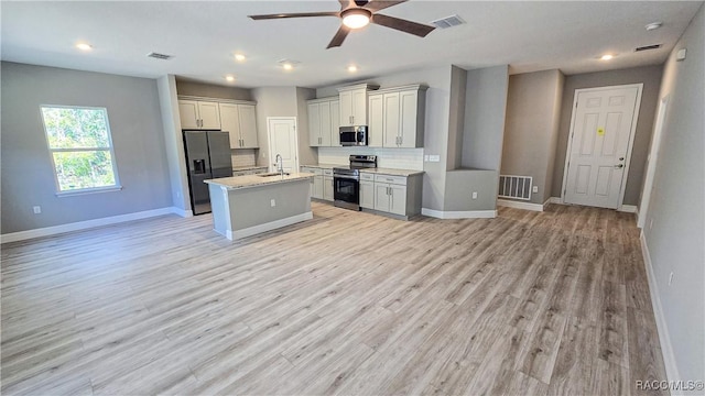 kitchen with sink, gray cabinets, appliances with stainless steel finishes, light stone counters, and an island with sink