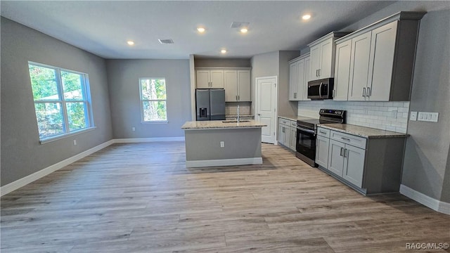 kitchen with range with electric cooktop, refrigerator with ice dispenser, light stone counters, and an island with sink