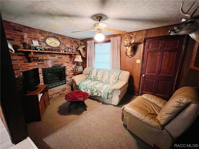 carpeted living room featuring ceiling fan, a textured ceiling, wooden walls, and a brick fireplace