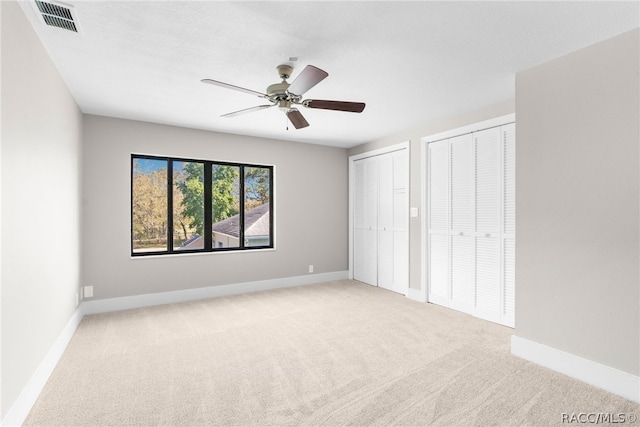 unfurnished bedroom featuring ceiling fan, light carpet, and two closets