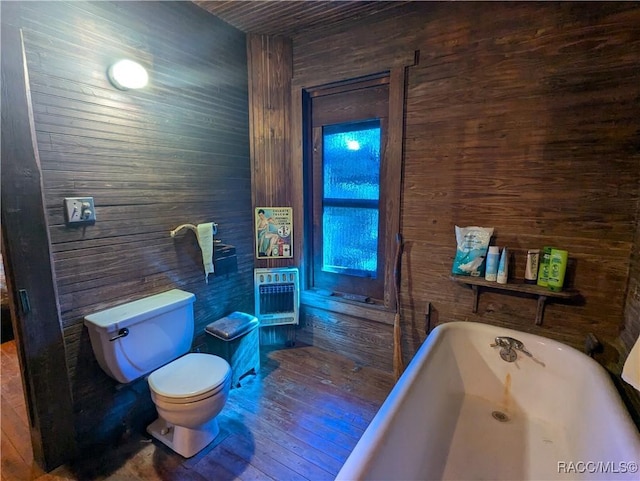 bathroom featuring hardwood / wood-style flooring, heating unit, a tub to relax in, toilet, and wood walls