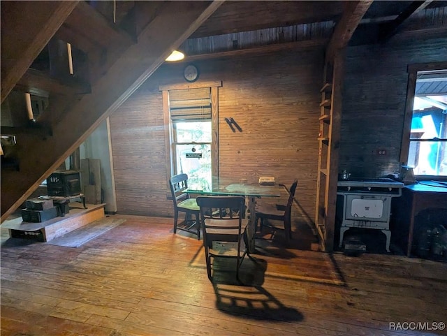 dining space featuring beam ceiling, a wealth of natural light, wooden walls, and wood-type flooring