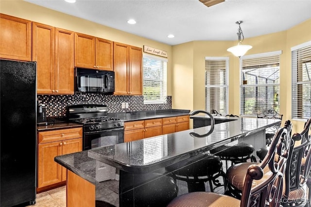 kitchen with a center island, a breakfast bar area, dark stone counters, hanging light fixtures, and black appliances