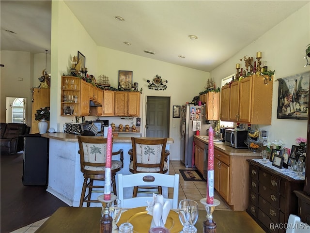 kitchen with stainless steel appliances, kitchen peninsula, lofted ceiling, a kitchen bar, and light tile patterned flooring