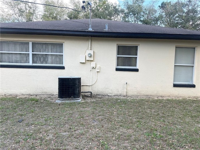 view of side of property with roof with shingles, central AC, and stucco siding