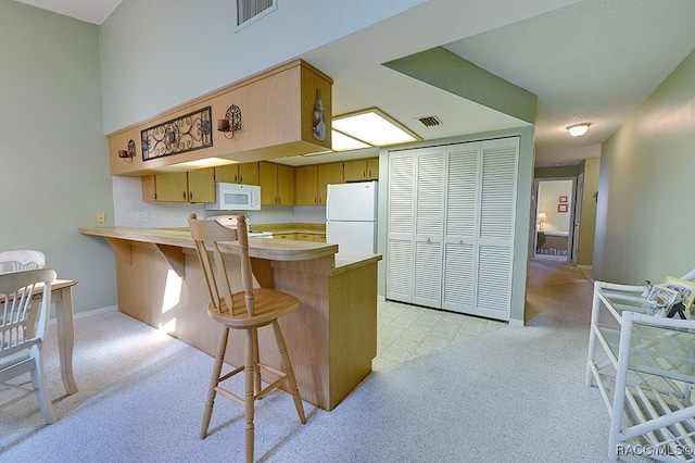 kitchen featuring kitchen peninsula, a kitchen breakfast bar, white appliances, and light carpet