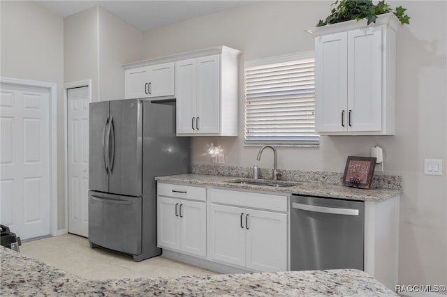 kitchen with light stone counters, stainless steel appliances, sink, white cabinetry, and light tile patterned flooring