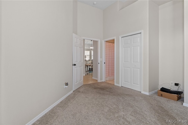 unfurnished bedroom featuring ensuite bathroom, light colored carpet, a towering ceiling, and a closet