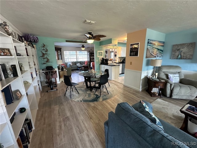 living room featuring ceiling fan, wood-type flooring, and a textured ceiling