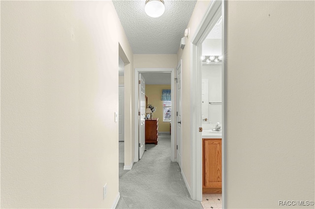 hall with sink, light colored carpet, and a textured ceiling