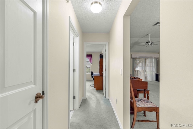 hall featuring a textured ceiling, light colored carpet, and a wealth of natural light