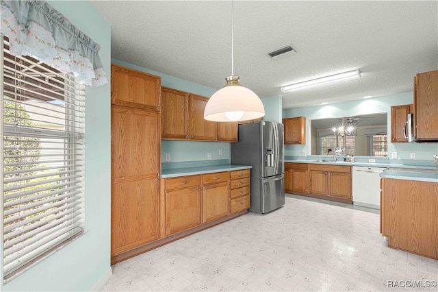 kitchen with a textured ceiling, sink, stainless steel appliances, and decorative light fixtures