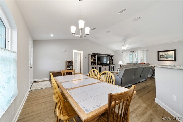 dining room featuring ceiling fan with notable chandelier, light wood-type flooring, and vaulted ceiling