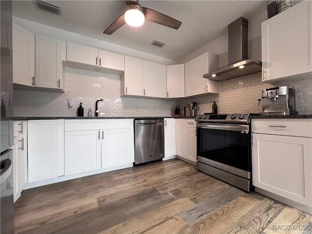 kitchen with wall chimney exhaust hood, appliances with stainless steel finishes, decorative backsplash, white cabinets, and hardwood / wood-style flooring