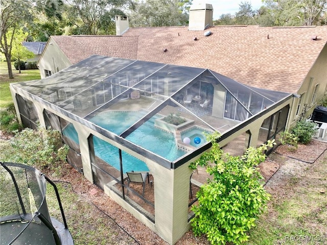 back of house featuring glass enclosure and an in ground hot tub