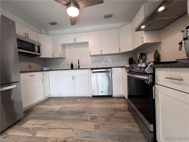 kitchen with backsplash, wall chimney exhaust hood, stainless steel appliances, white cabinets, and light hardwood / wood-style floors