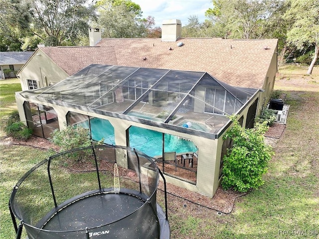 rear view of property with glass enclosure and an in ground hot tub