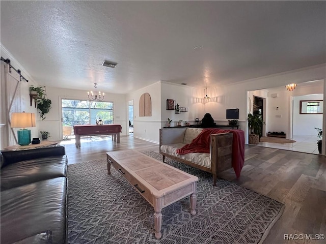 living room with a barn door, billiards, a notable chandelier, wood-type flooring, and a textured ceiling