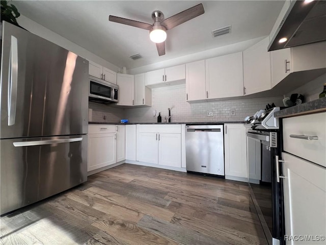 kitchen featuring ventilation hood, decorative backsplash, white cabinetry, wood-type flooring, and stainless steel appliances