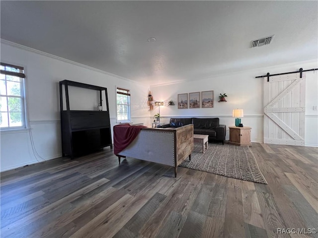 living room with a barn door, wood-type flooring, and crown molding