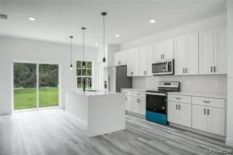 kitchen featuring stainless steel appliances, sink, white cabinets, a center island, and hanging light fixtures