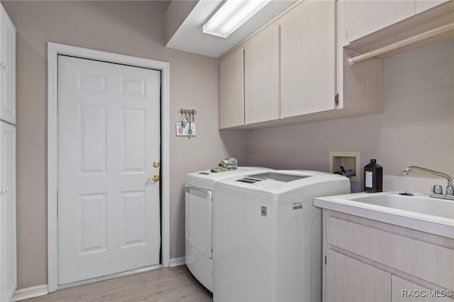 washroom featuring light wood-type flooring, cabinet space, washer and clothes dryer, and a sink