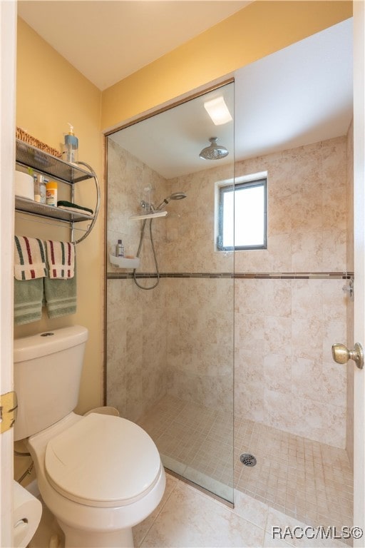 bathroom with toilet, tile patterned flooring, and tiled shower