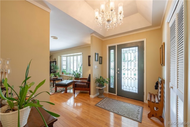 entryway featuring a raised ceiling, light hardwood / wood-style flooring, ornamental molding, and an inviting chandelier