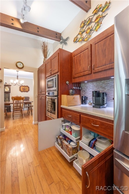 kitchen featuring stainless steel appliances, beamed ceiling, a notable chandelier, decorative light fixtures, and light wood-type flooring