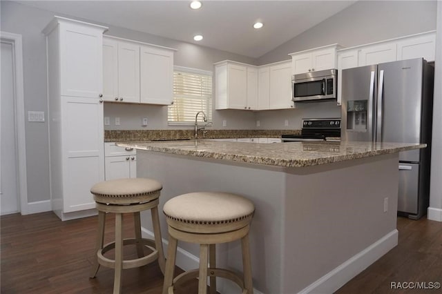 kitchen with lofted ceiling, appliances with stainless steel finishes, a kitchen island, and white cabinets