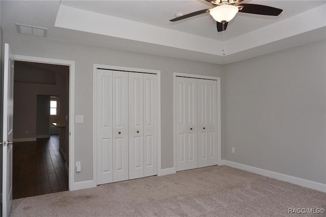 unfurnished bedroom featuring multiple closets, carpet floors, a raised ceiling, and ceiling fan