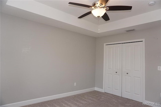 unfurnished bedroom with a tray ceiling, a closet, ceiling fan, and carpet flooring