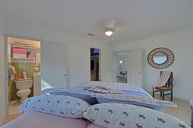 bedroom with ensuite bathroom, a walk in closet, tile walls, light tile patterned floors, and a closet