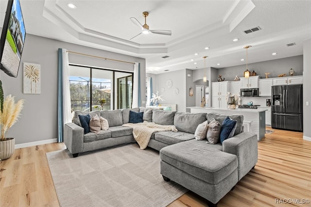 living room featuring ceiling fan, light hardwood / wood-style floors, and a raised ceiling