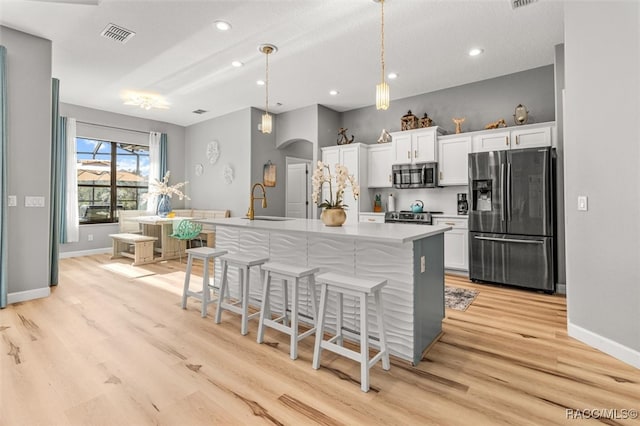 kitchen featuring a breakfast bar, white cabinetry, a center island with sink, and appliances with stainless steel finishes