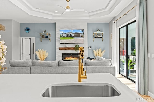 living room with a raised ceiling, ceiling fan, and sink