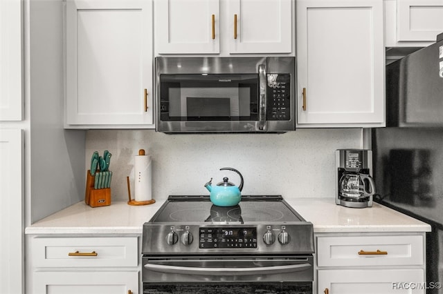 kitchen featuring appliances with stainless steel finishes, backsplash, white cabinetry, and light stone counters