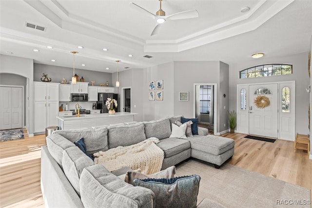 living room with a raised ceiling, ceiling fan, light hardwood / wood-style flooring, and a towering ceiling