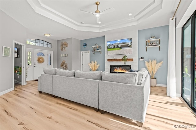 living room featuring ceiling fan, light hardwood / wood-style floors, a wealth of natural light, and a tray ceiling