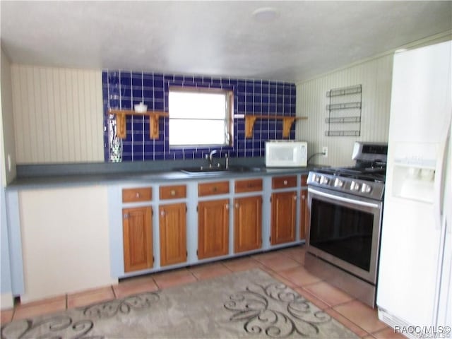 kitchen with brown cabinetry, white appliances, a sink, and light tile patterned floors