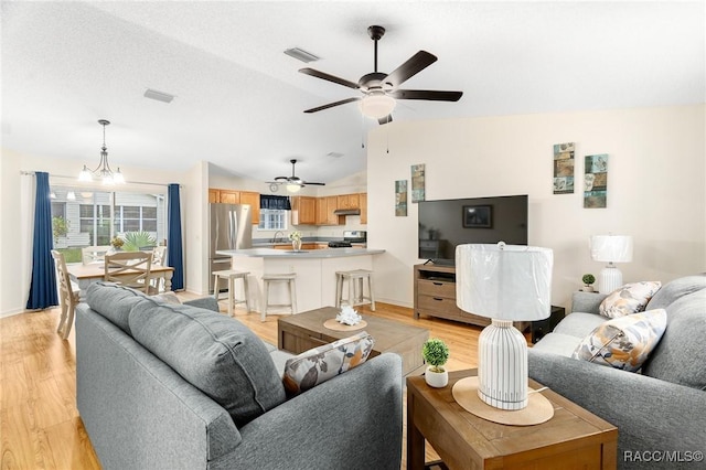 living room featuring sink, vaulted ceiling, a textured ceiling, light hardwood / wood-style floors, and ceiling fan with notable chandelier