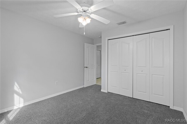 unfurnished bedroom with ceiling fan, a closet, and dark carpet