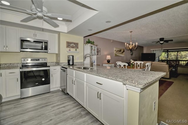 kitchen featuring open floor plan, a peninsula, stainless steel appliances, white cabinetry, and a sink