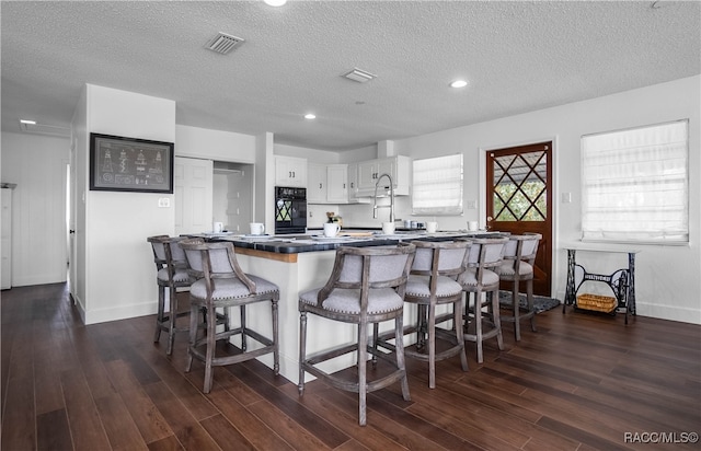 kitchen featuring black oven, dark hardwood / wood-style floors, white cabinetry, and a textured ceiling