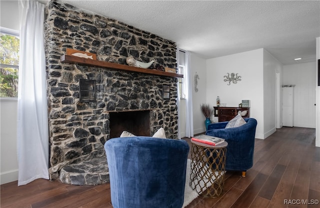 living room featuring dark hardwood / wood-style floors, a stone fireplace, and a textured ceiling