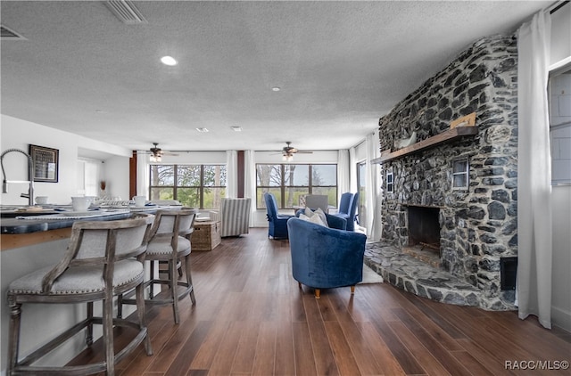 living room with a fireplace, a textured ceiling, ceiling fan, and dark wood-type flooring