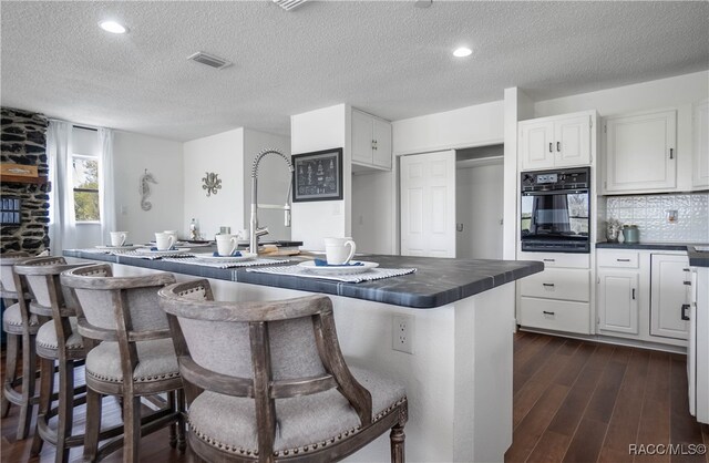 kitchen featuring a breakfast bar, dark wood-type flooring, white cabinets, a textured ceiling, and black oven