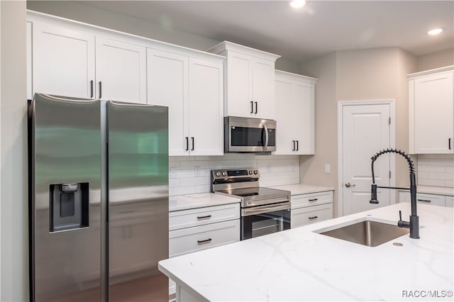 kitchen featuring appliances with stainless steel finishes, light stone counters, white cabinetry, and sink