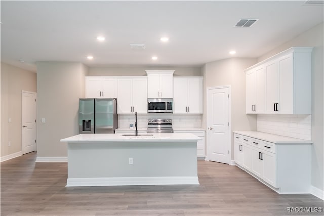 kitchen with stainless steel appliances, white cabinetry, light hardwood / wood-style floors, and an island with sink