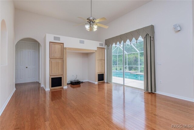unfurnished living room with light wood finished floors, a ceiling fan, arched walkways, baseboards, and high vaulted ceiling